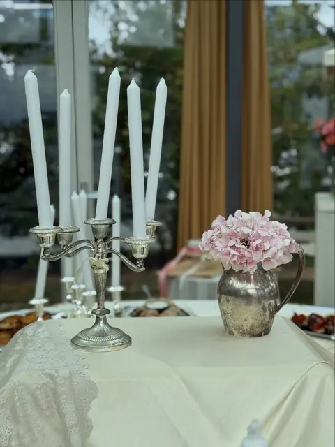 Witte tafel met kandelaars en roze bloemen in een lichte serre