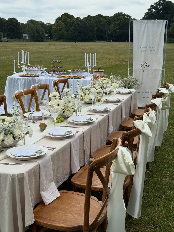 Lange brunchtafel met wit tafellinnen en gevulde schalen, buiten in het park