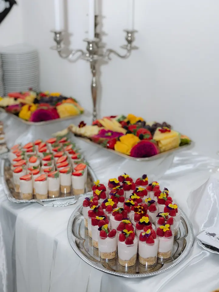 Cheesecakecups met rood fruit en eetbare bloemen op zilveren schalen, met fruitschalen op de achtergrond