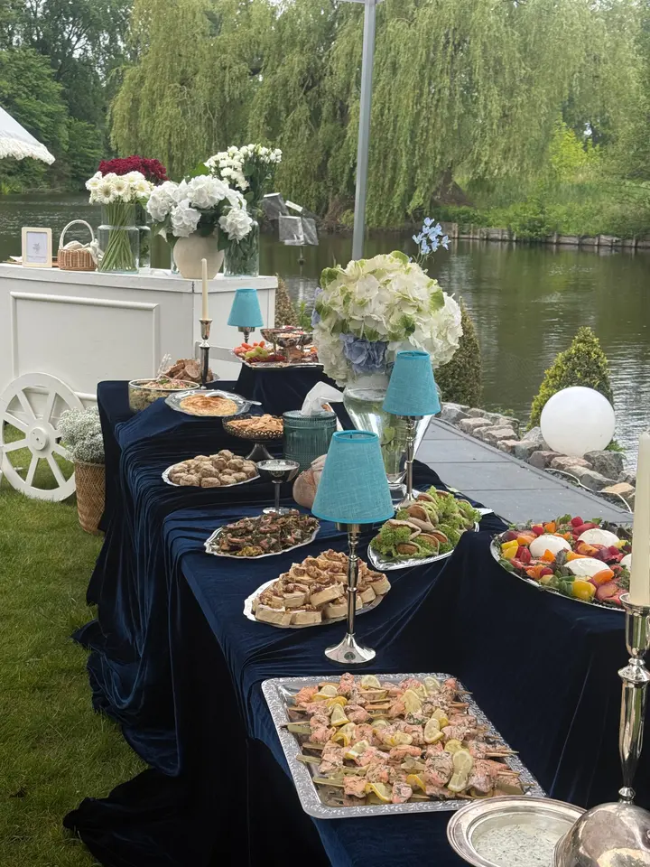 Lunchbuffet op blauw fluweel met schalen vol hapjes en bloemen, aan het water