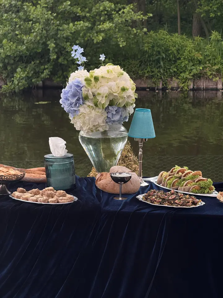 Lunchtafel met donkerblauw fluweel, witte hortensia's en zilveren schalen vol hapjes, buiten aan het water